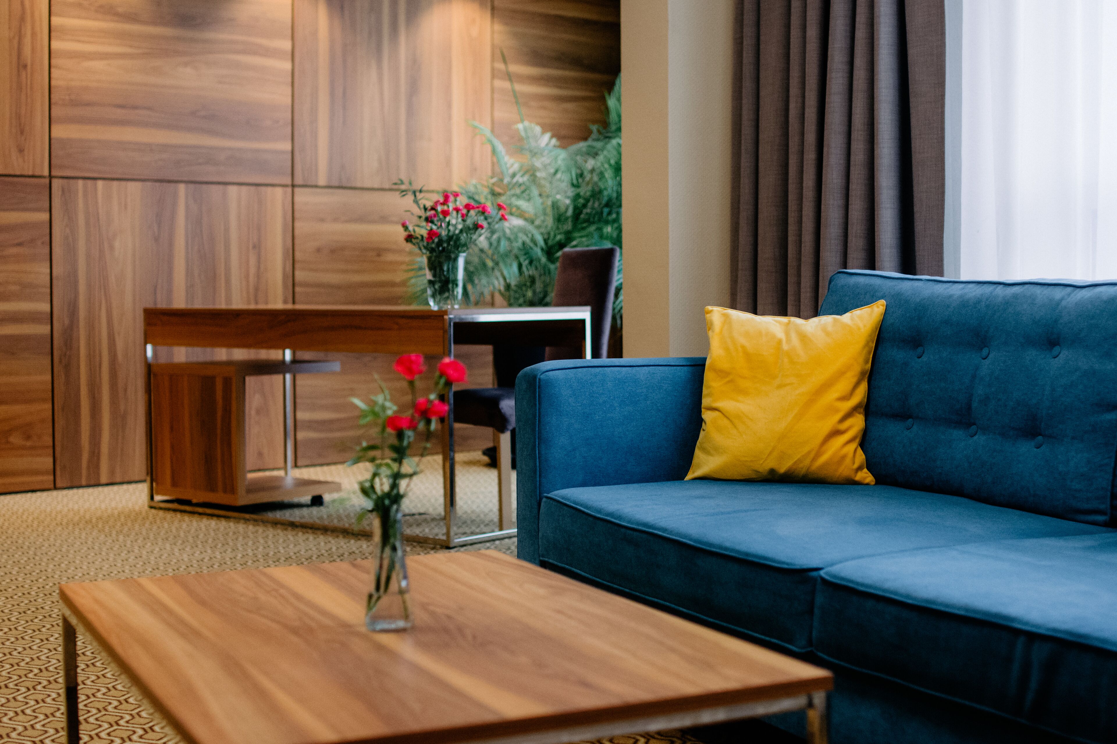 Un salon moderne avec un canapé bleu, une table basse en bois et un vase rempli de fleurs rouges.