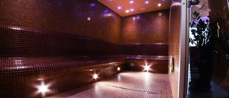 Un cuarto de spa con paredes y piso de baldosas, un banco e iluminación empotrada en el techo.