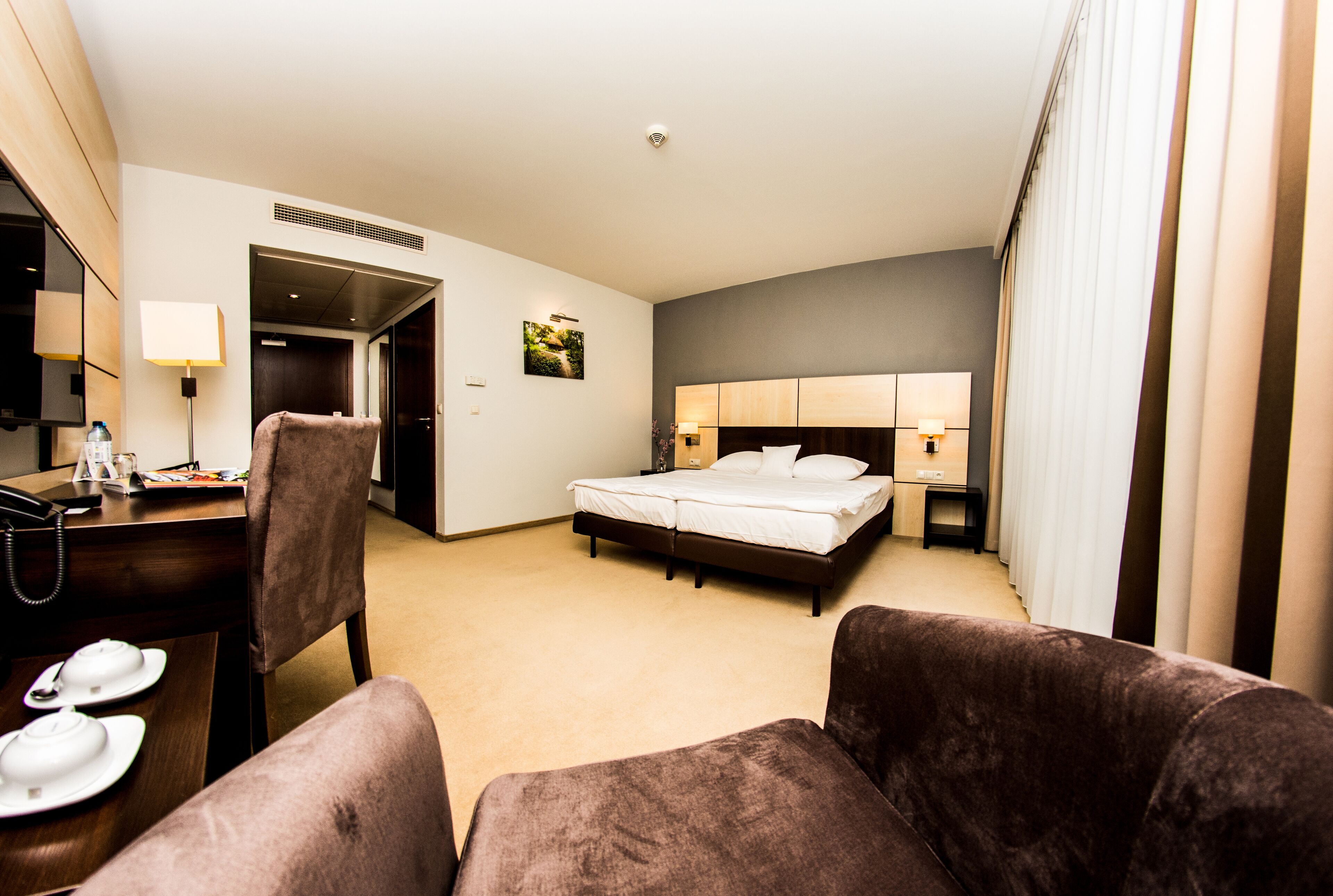 A hotel room with a bed, a desk with a telephone, a chair, and a couch.