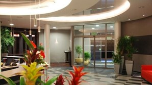 A modern lobby with a reception desk, potted plants, and a red seating area. - Ruben Hotel (Zielona Gora)