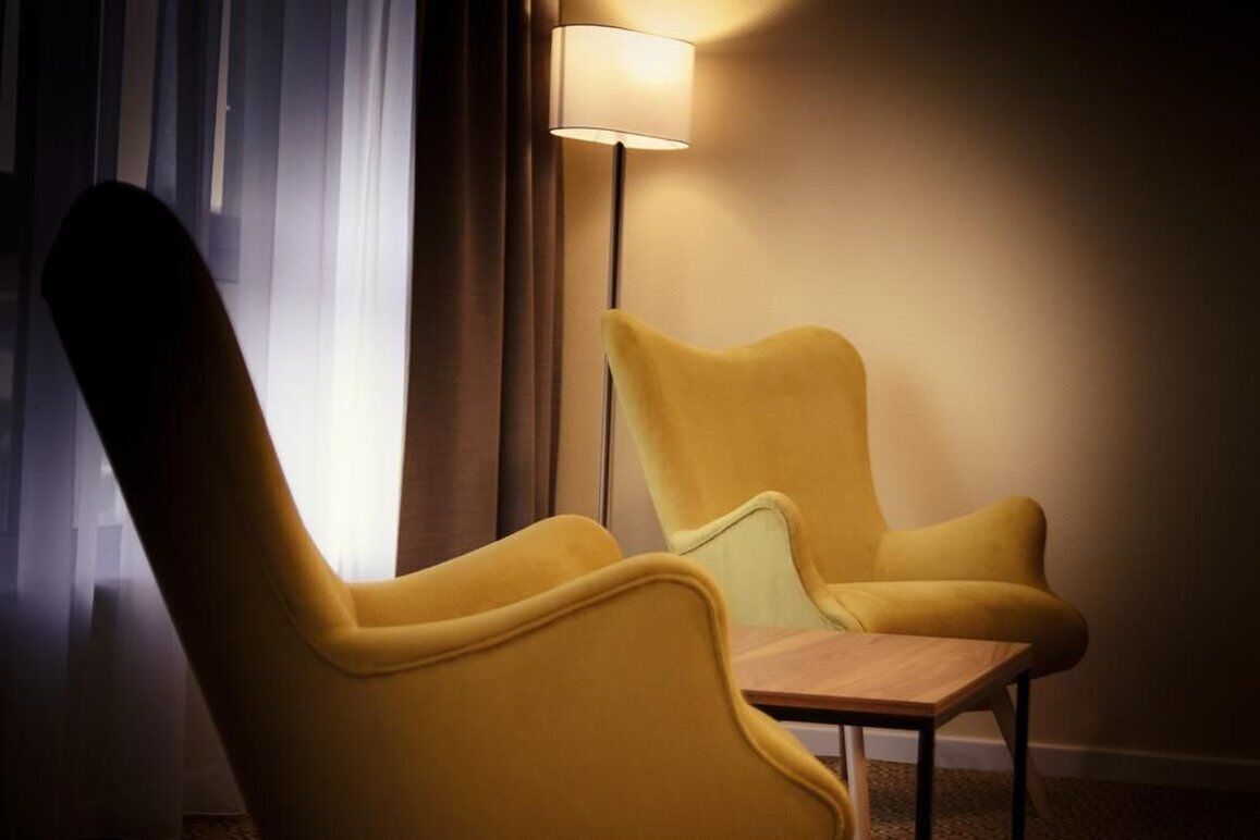 A room with two yellow armchairs and a small wooden table. A floor lamp provides lighting.