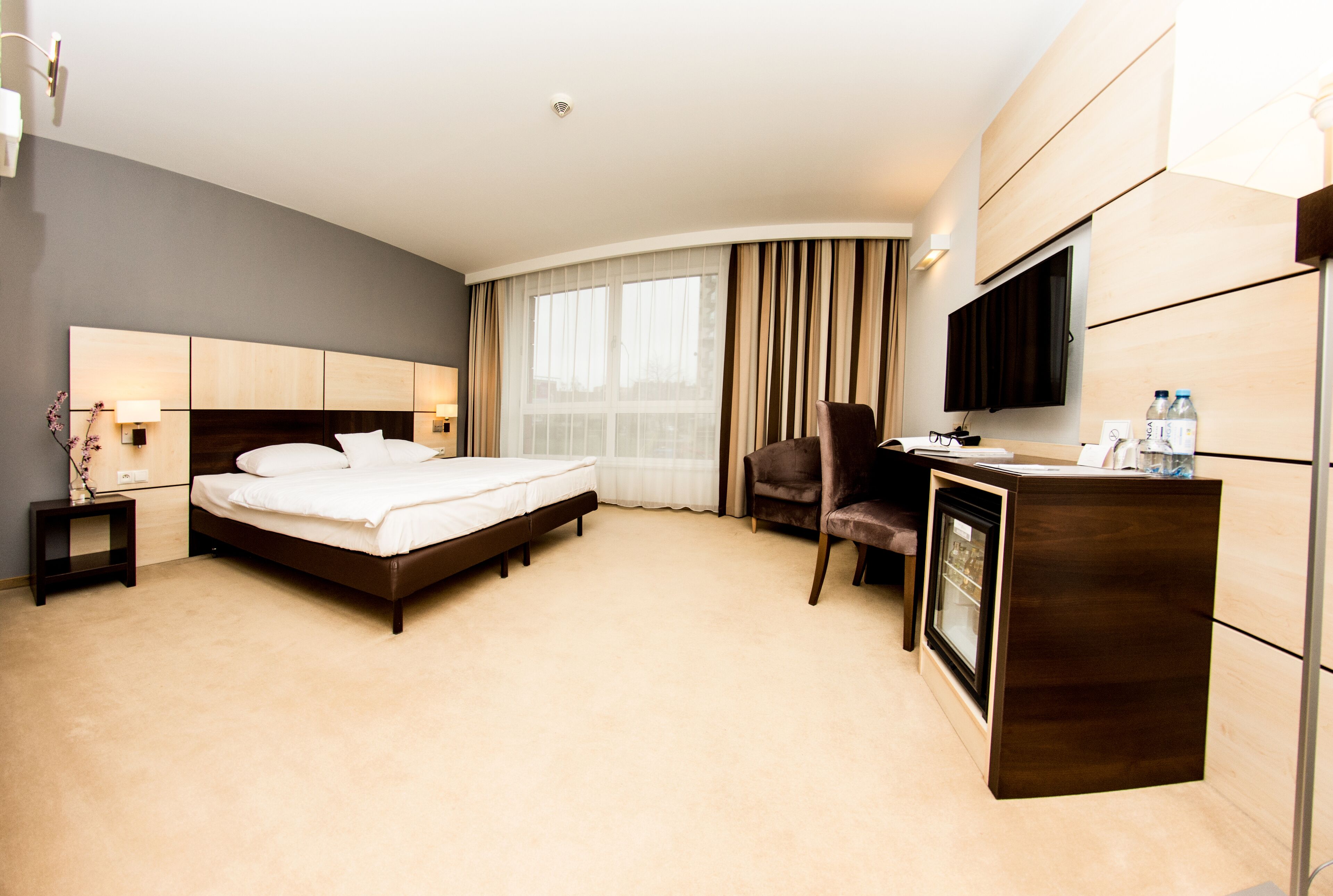 Habitación de hotel con cama, escritorio, silla, televisión y minibar.