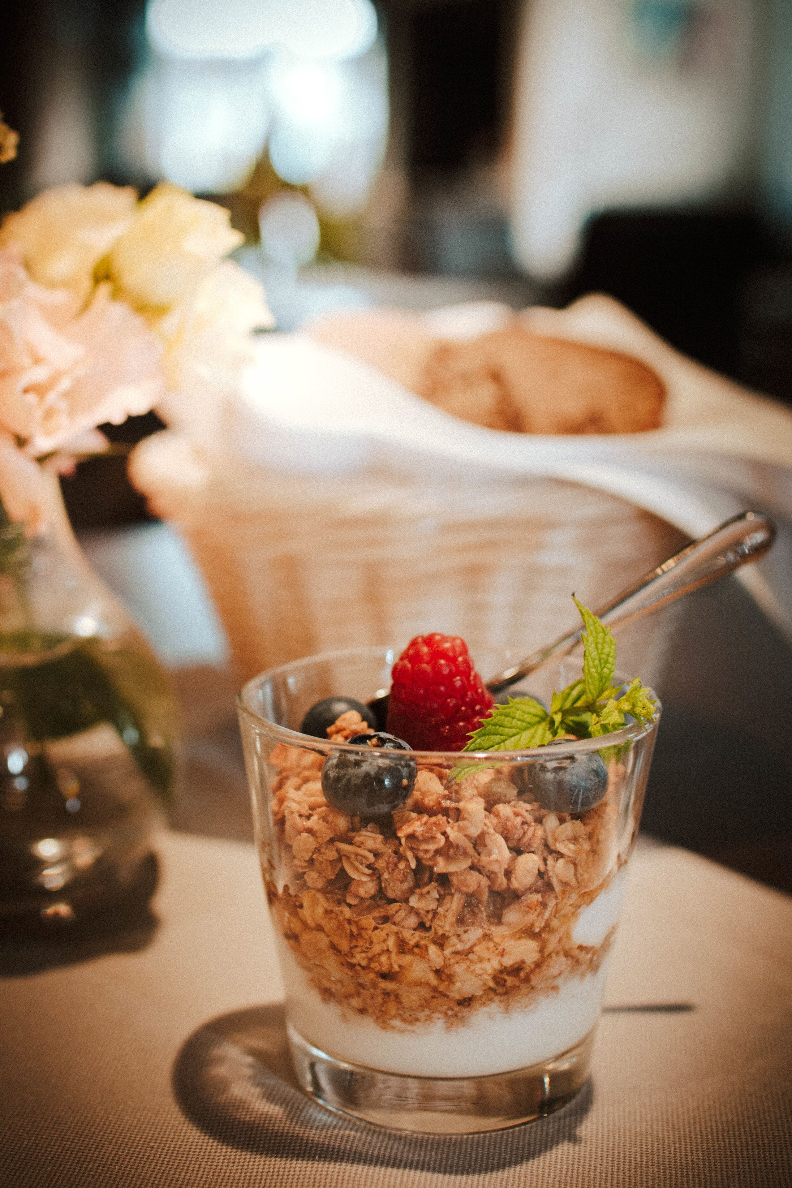 Un vaso de vidrio con un parfait de yogur, granola, frambuesas y arándanos, acompañado de una cuchara.