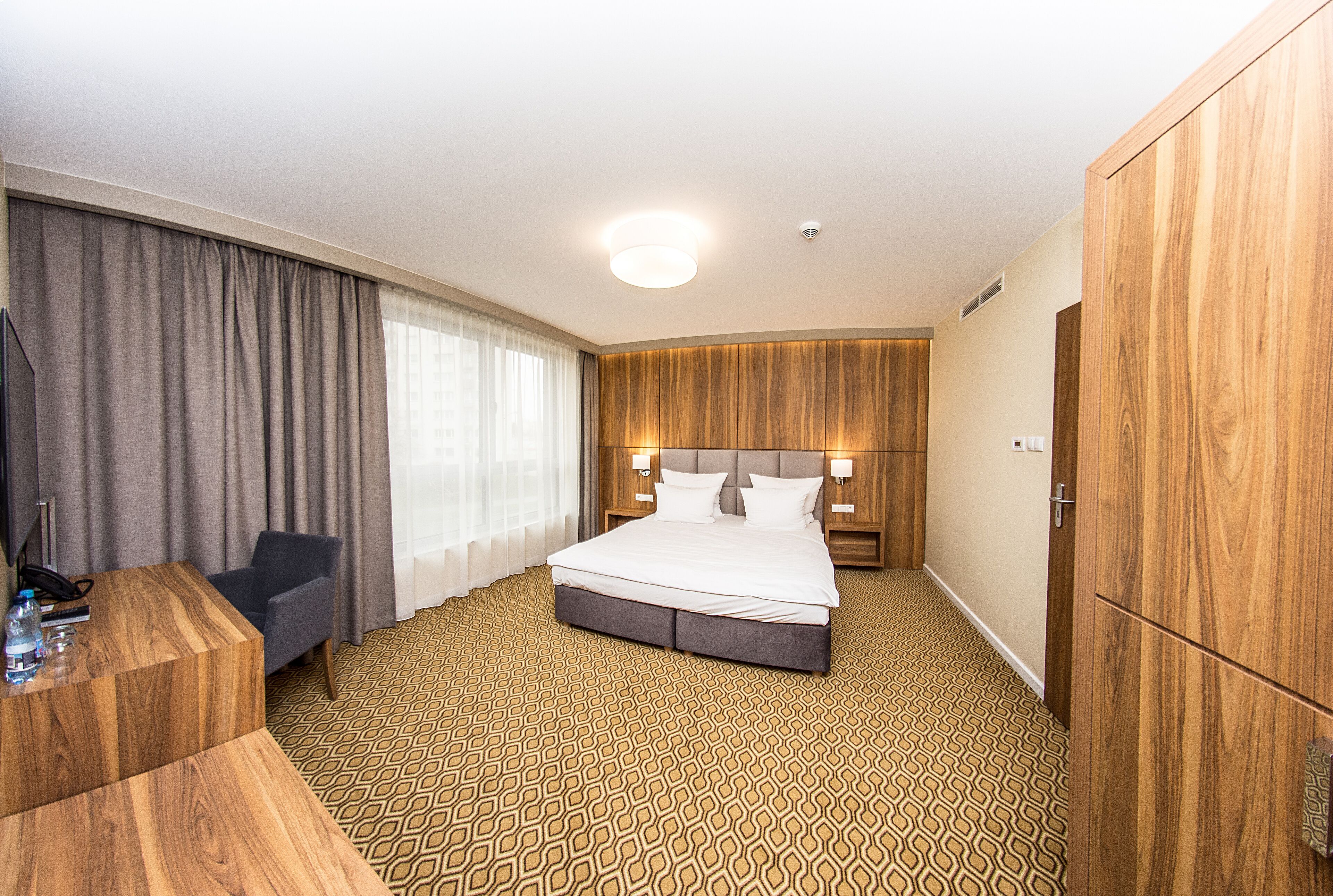Una habitación de hotel con una cama grande, un escritorio, una silla y un armario.
