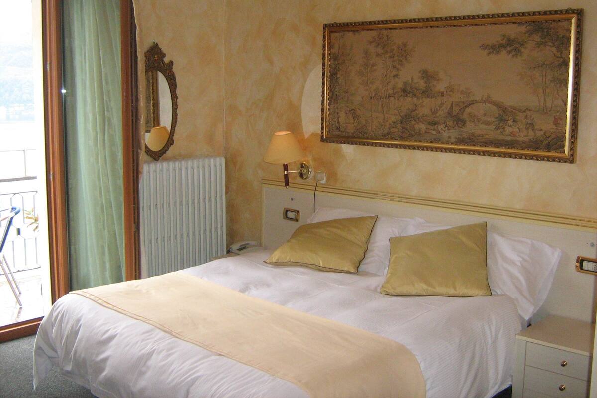 A hotel room with a bed, a nightstand, a lamp, a painting, and a window with curtains.