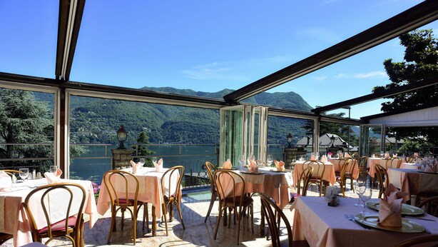 A restaurant with tables set for dining, overlooking a lake and mountains. - San Marino (Laglio)