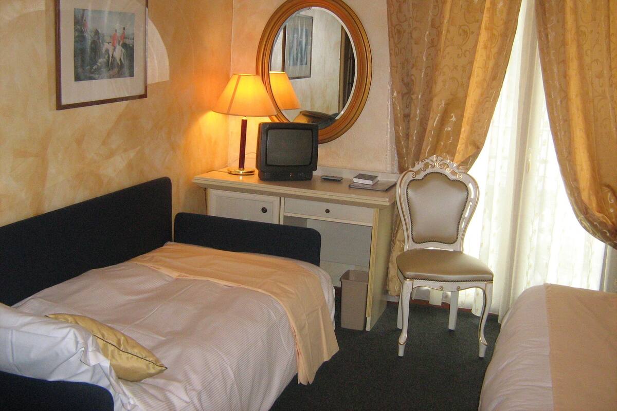 A hotel room with a bed, a desk with a computer, a chair, and a mirror.