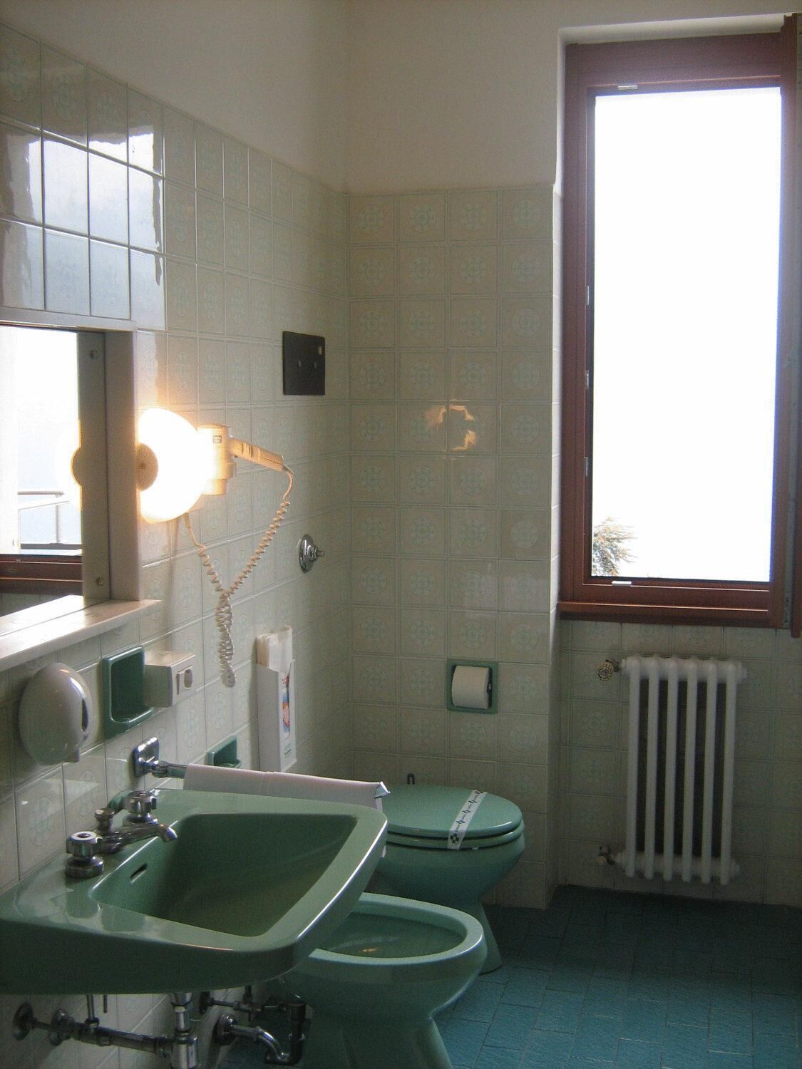 Ein Badezimmer mit einem grünen Waschbecken, einer Toilette, einem Spiegel und einem Fenster.