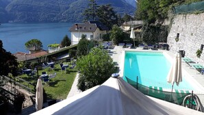 A pool area with lounge chairs and umbrellas, overlooking a lake with mountains in the background. - San Marino (Laglio)