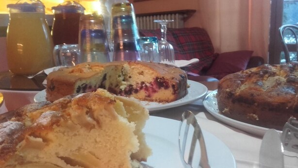 A table with various baked goods, including cakes and pastries, in a dining area. - San Marino (Laglio)