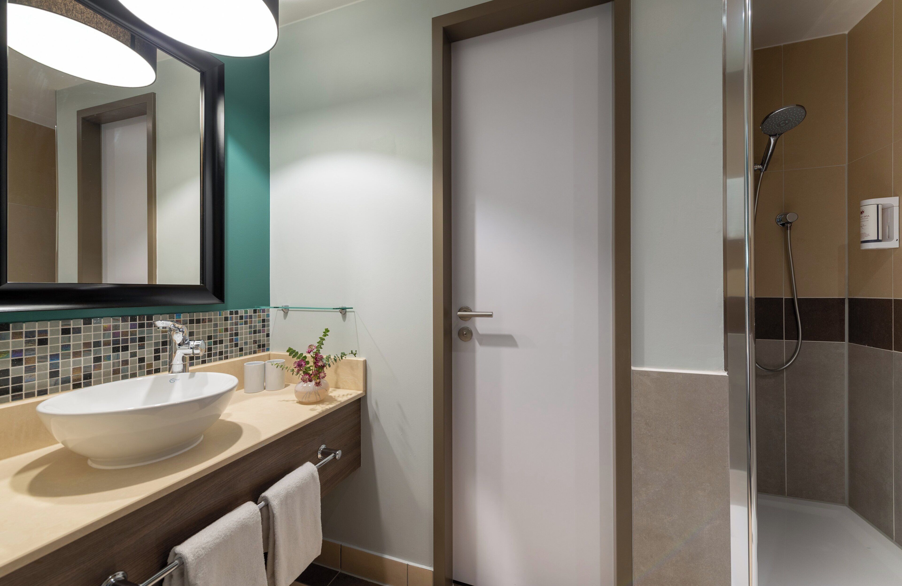 Une salle de bain moderne avec un grand lavabo ovale, une douche en verre et un miroir doté d’un cadre de couleur turquoise.