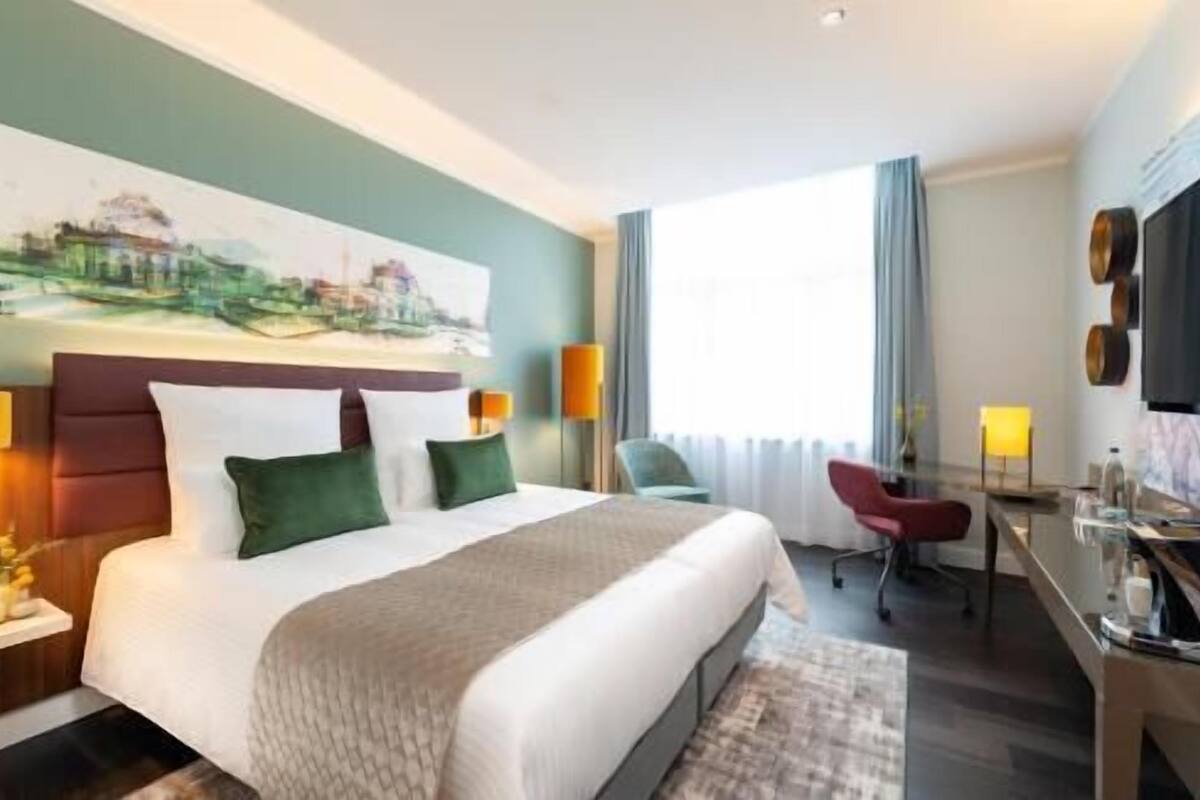 Una habitación de hotel con una cama grande, un escritorio, una silla y un cuadro en la pared.