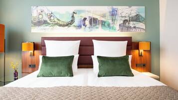 A hotel room with a large bed, two green pillows, a headboard, and a wall art piece above the bed.