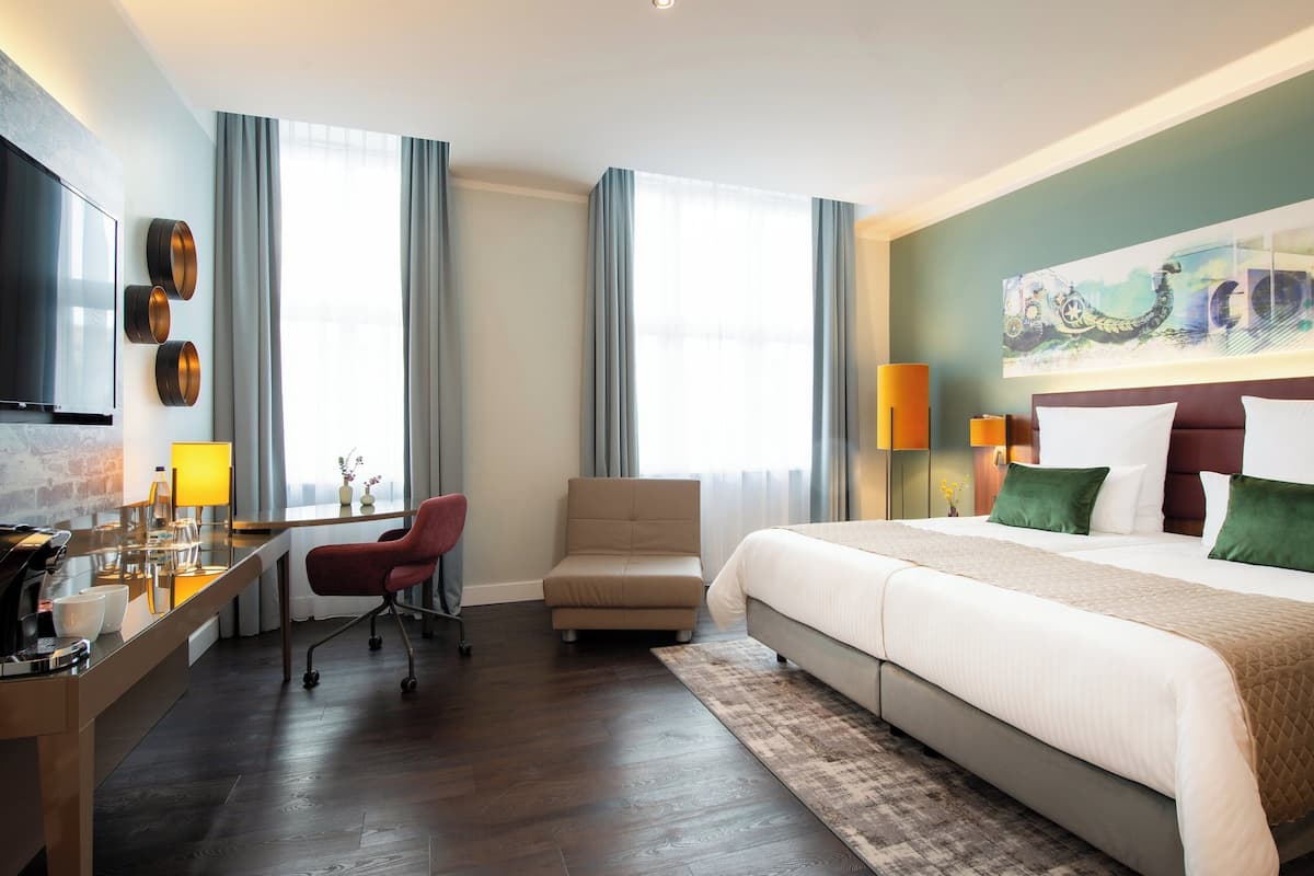 A hotel room with a large bed, a desk with a chair, a TV, and a painting on the wall.