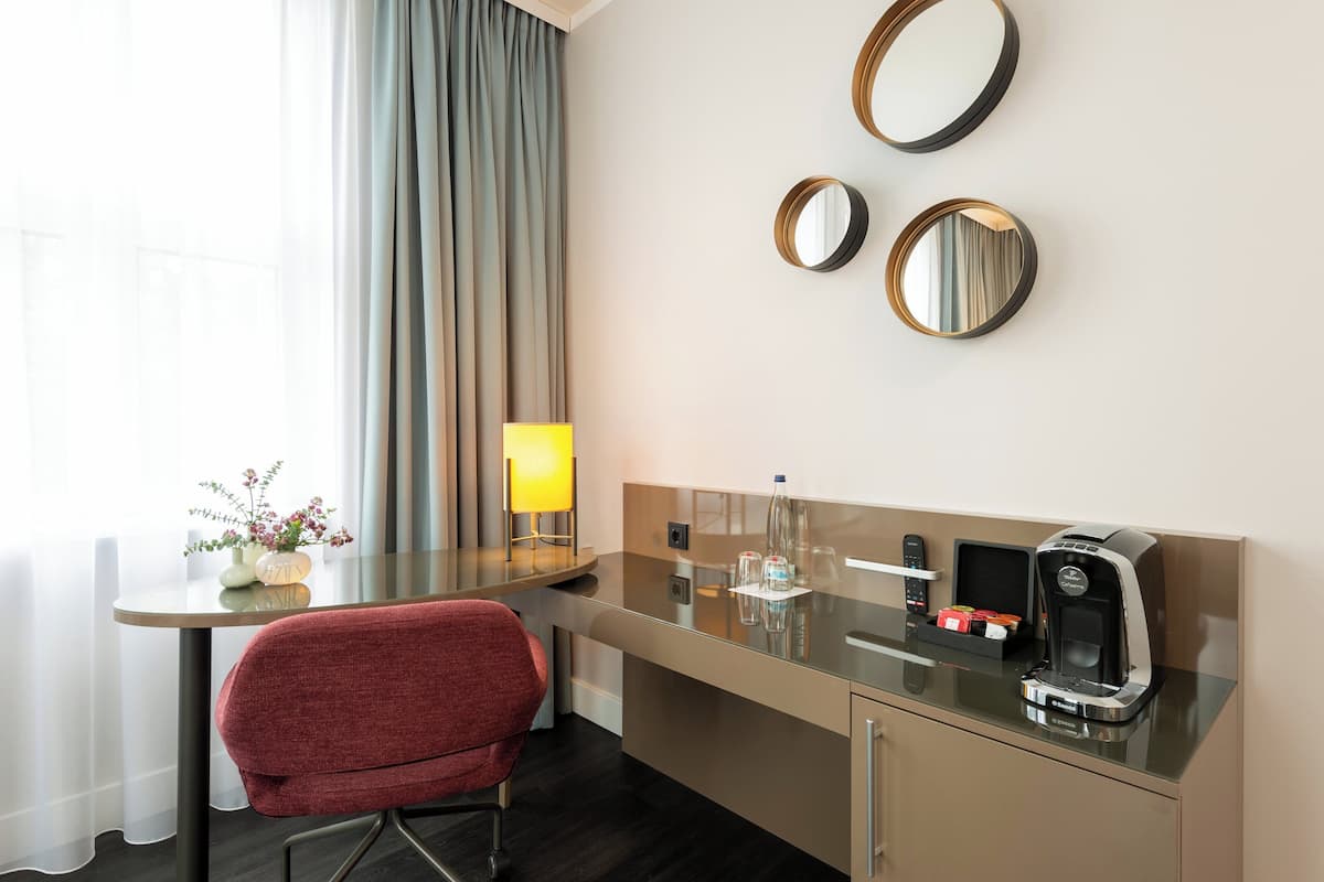 A hotel room with a desk, a chair, a coffee machine, and two wall-mounted mirrors.