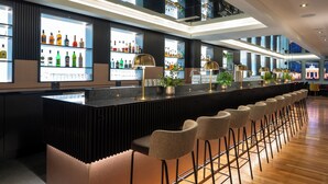 A modern bar area with a long counter, multiple shelves of bottles, and several bar stools. - Leonardo Royal Hotel Berlin Alexanderplatz (Berlin)