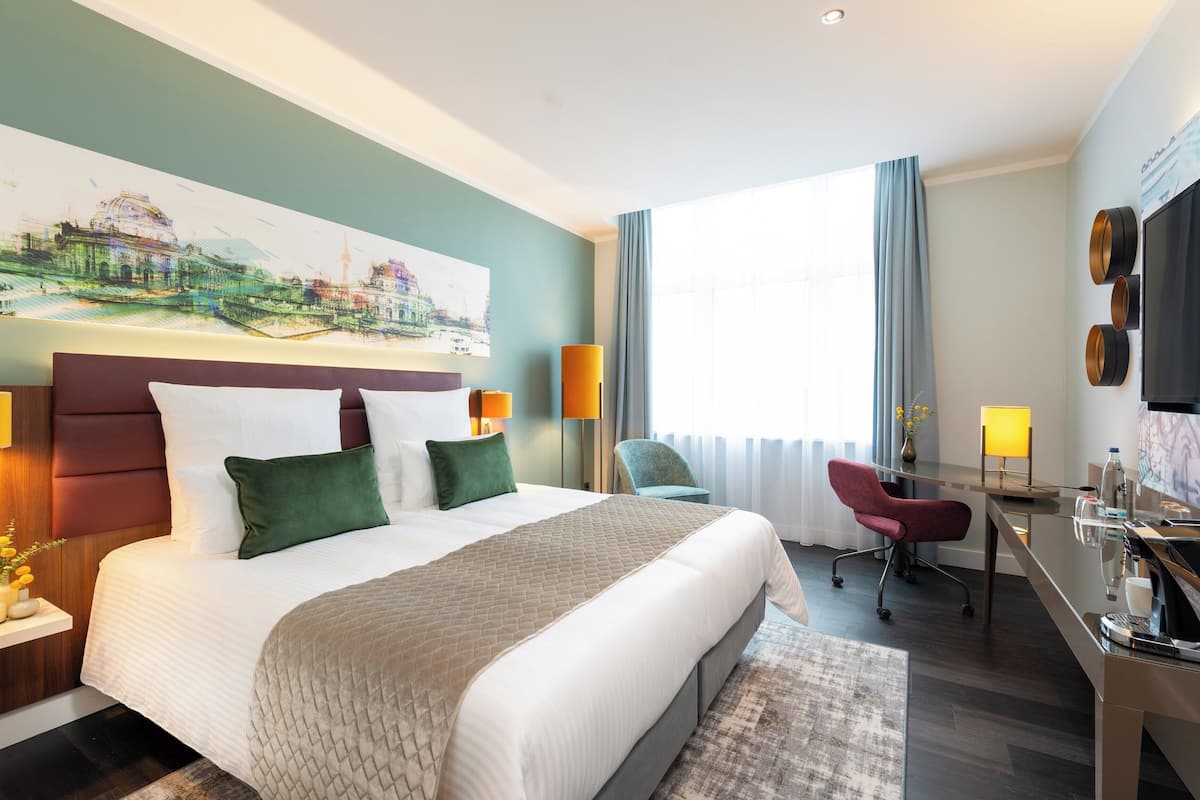 A hotel room with a large bed, a desk, a chair, and a TV.
