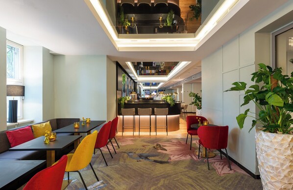 A modern hotel lobby with a central bar area, seating arrangements, and a large potted plant.
