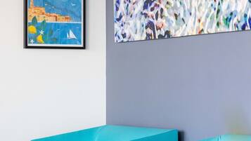 A room with two teal chairs, a framed picture of Menton, Riviera & Merveilles, and a large abstract painting.