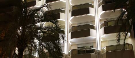 A multi-story hotel with balconies, a palm tree, and a neon sign.