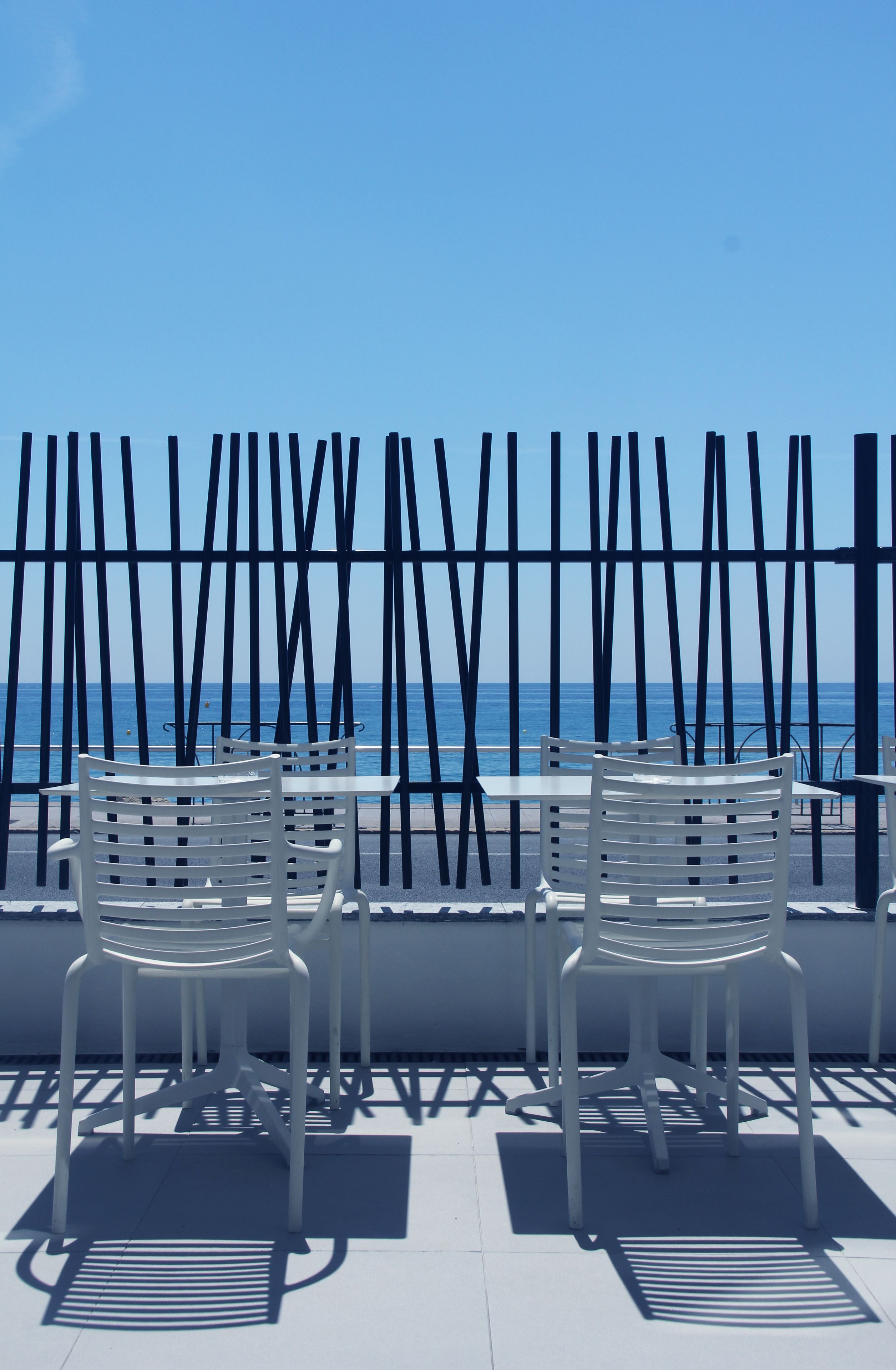 Una terraza con sillas y mesas blancas, con vista al mar.