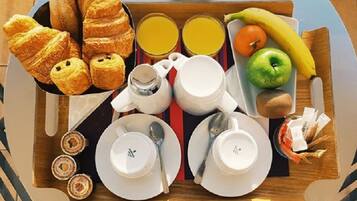 Un plateau de petit-déjeuner avec des croissants, du jus, une banane, une pomme et des tasses de café.
