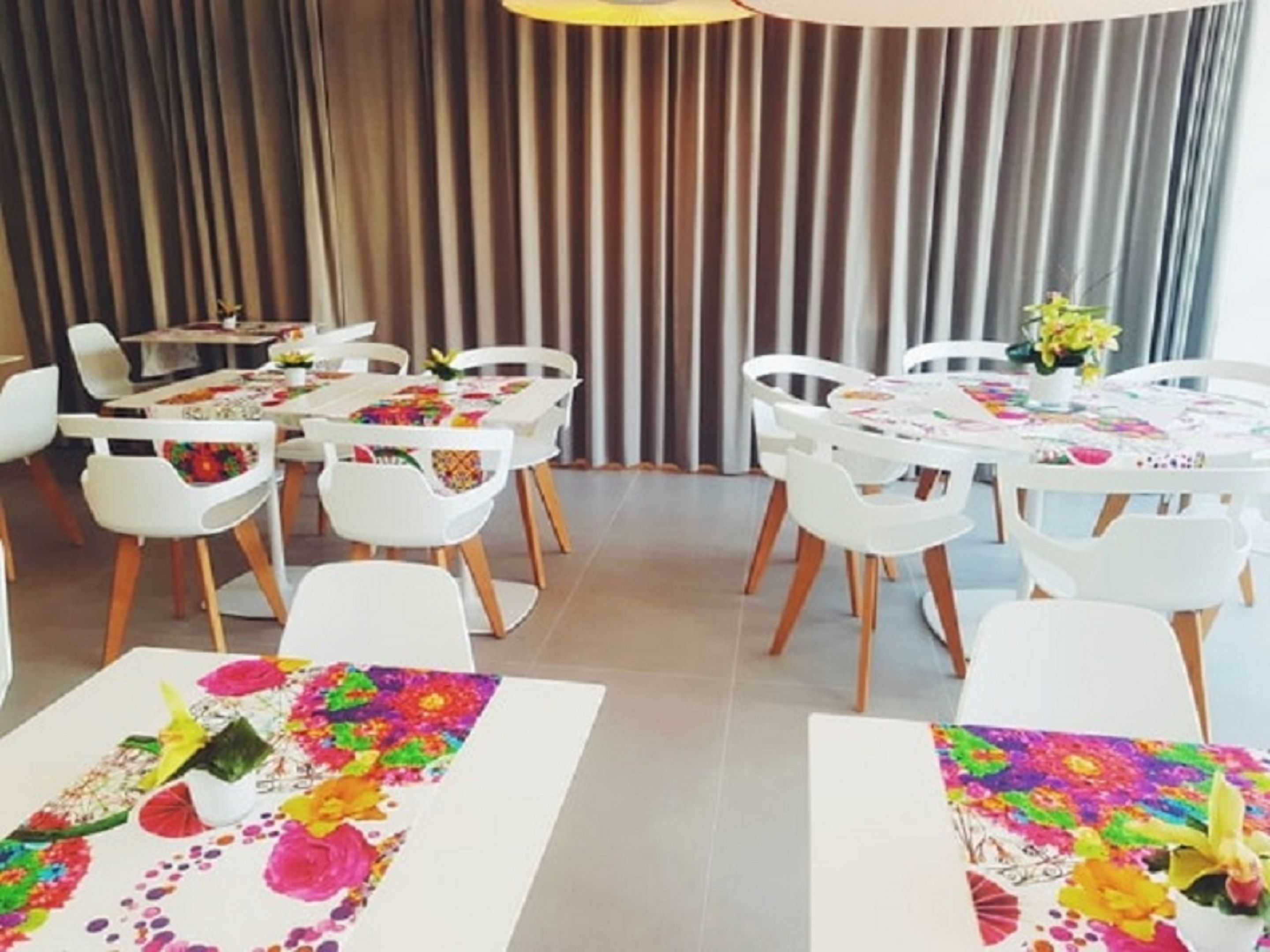 Un comedor con sillas y mesas blancas, cada una con manteles coloridos y centros de mesa florales.