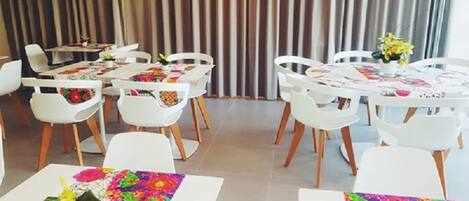 Un comedor con sillas y mesas blancas, cada una con manteles coloridos y centros de mesa florales.