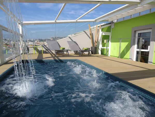 A rooftop pool area with a view of the city, lounge chairs, and a green wall.