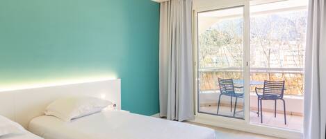 Habitación de hotel con dos camas, un ventanal con vistas a sillas y árboles al aire libre, y una pared de acento color turquesa.