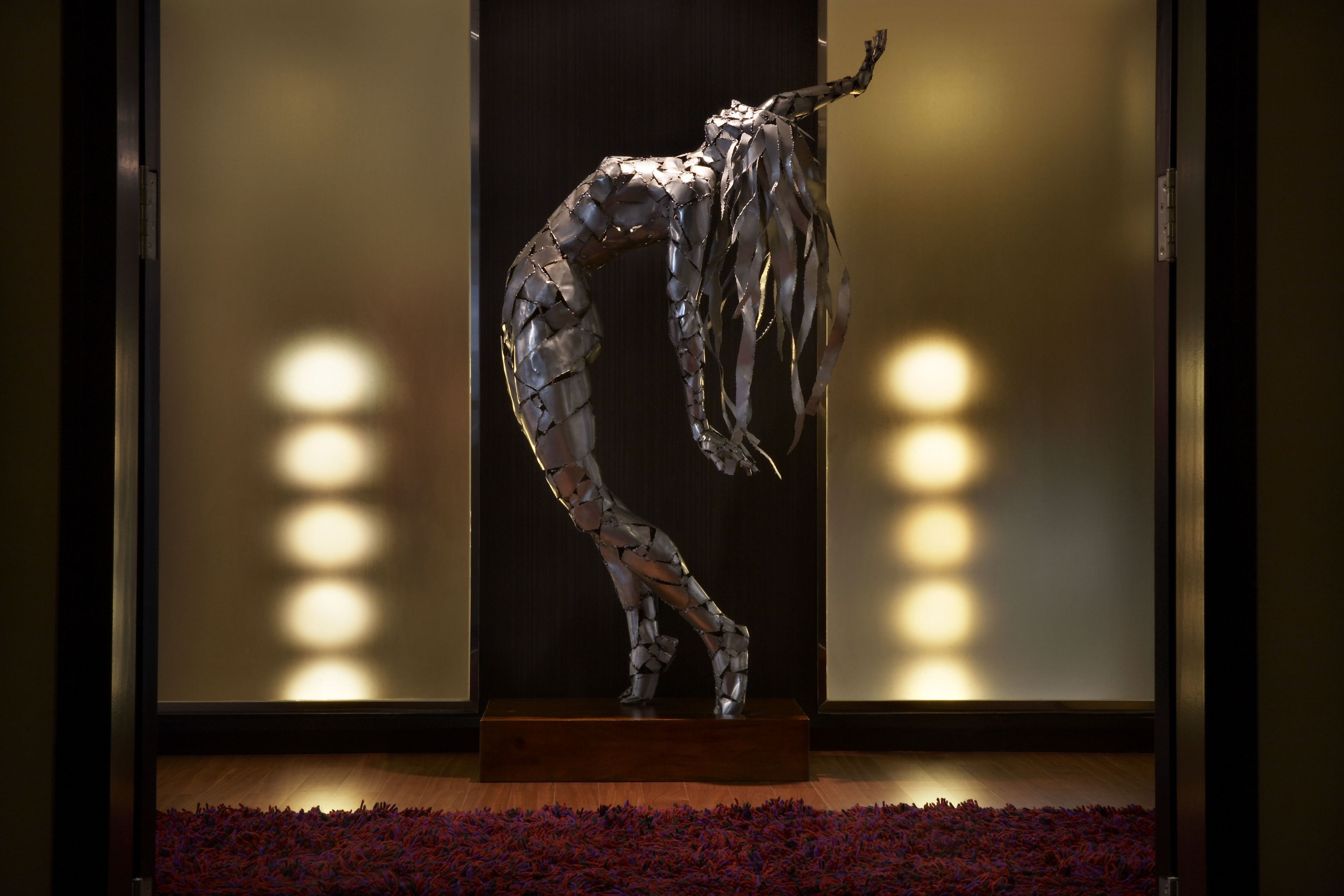 Une sculpture dans un hall d’entrée moderne, avec un plancher en bois et un fond sombre.