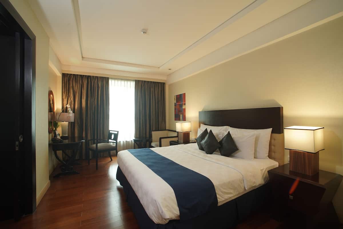 A hotel room with a bed, bedside tables, a desk, a chair, and a view of the outdoors.