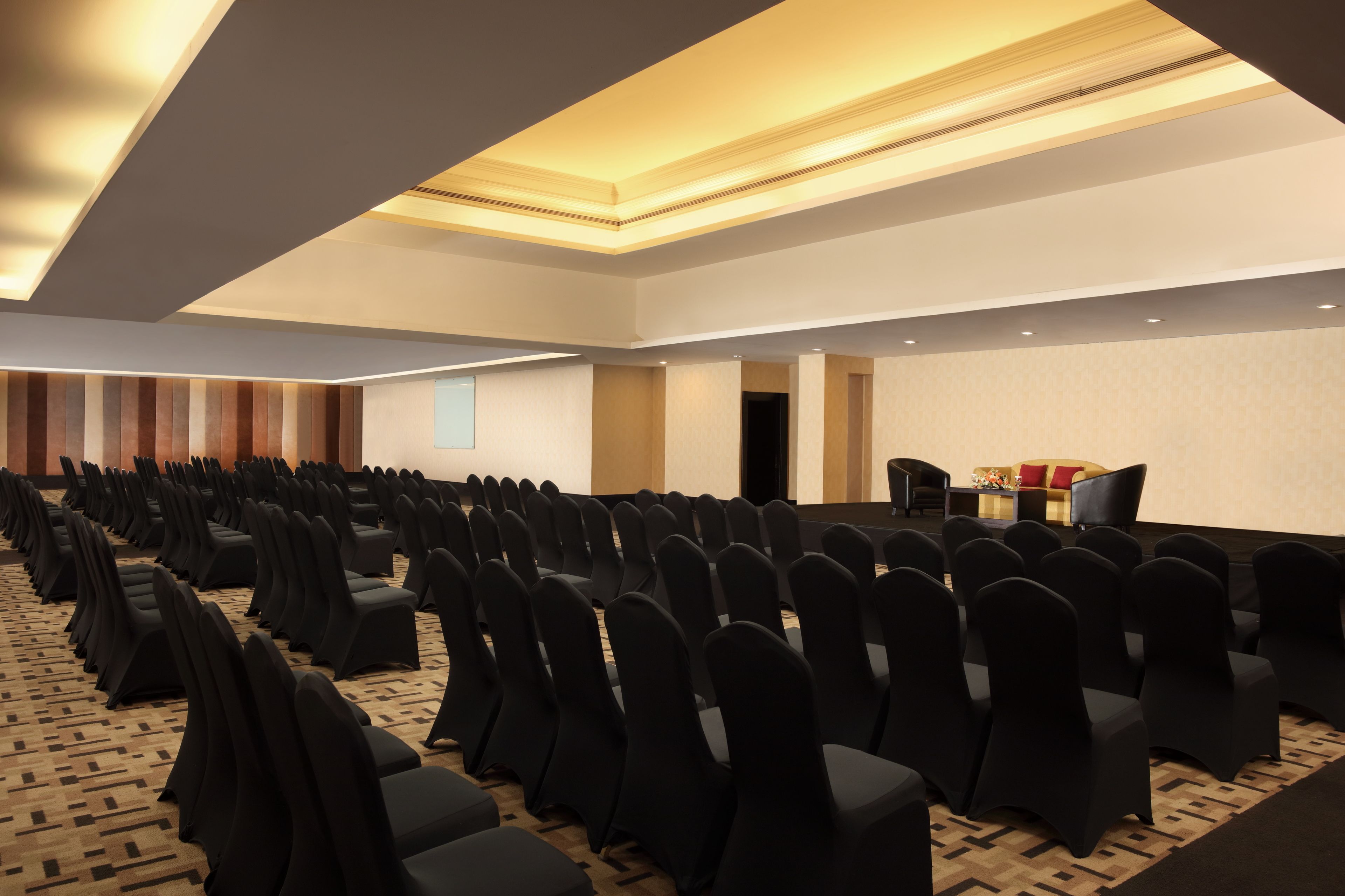 Un salón de conferencias con filas de sillas negras y un escenario.
