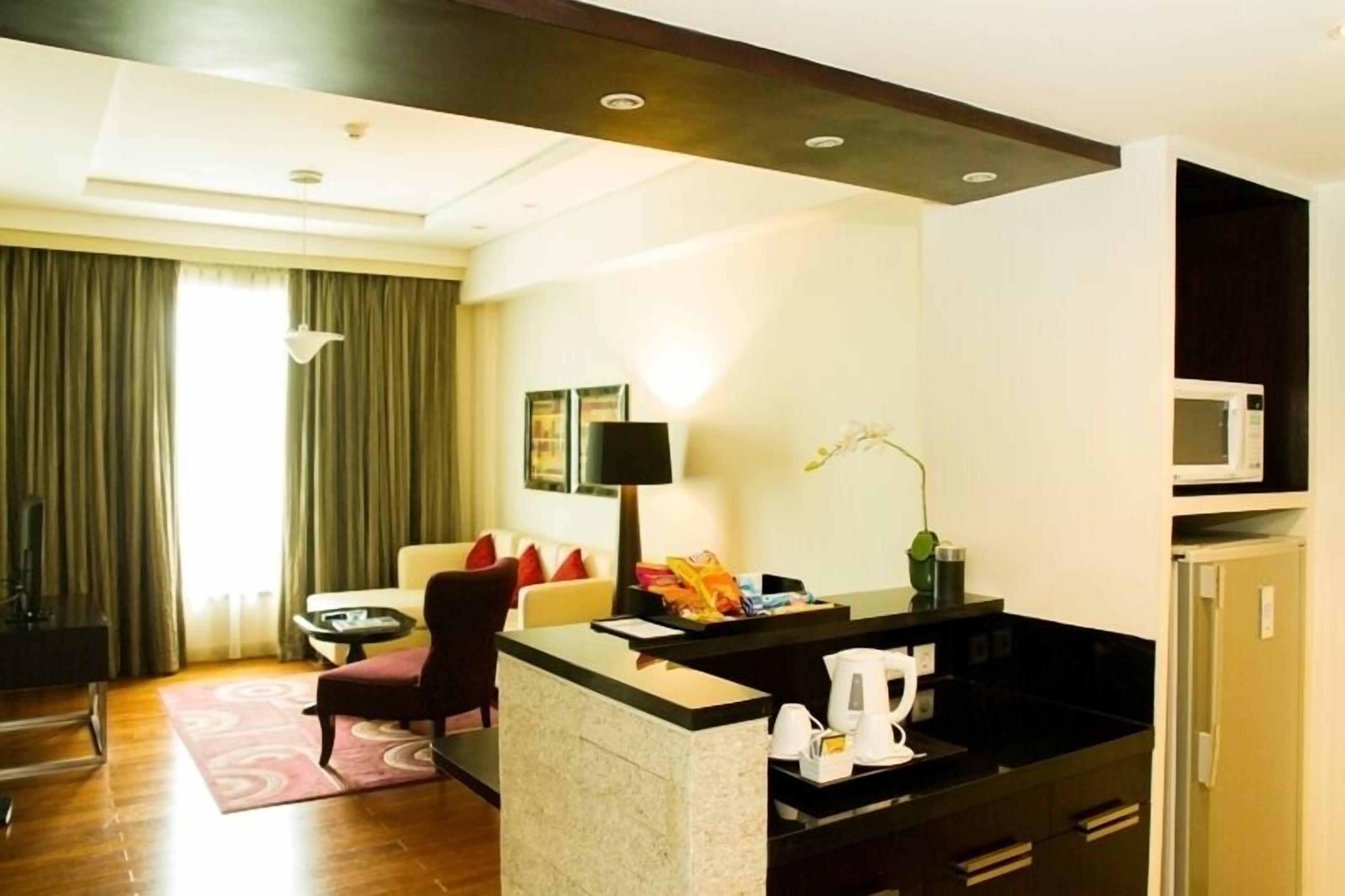 A hotel room with a living area, a small kitchen, a sofa, a coffee table, and a dining table.