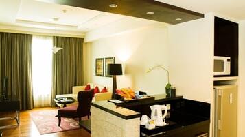 A hotel room with a living area, a small kitchen, a sofa, a coffee table, and a dining table.