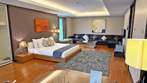 A modern hotel room with a bed, sofa, and a dining area.