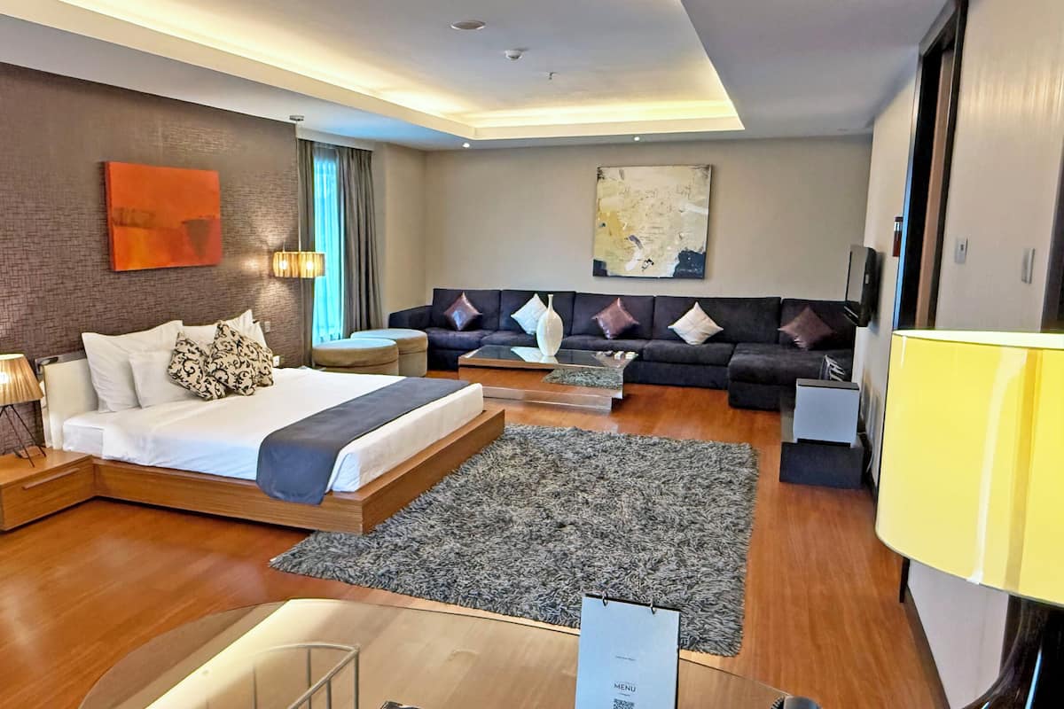 A modern hotel room with a bed, sofa, and a dining area.
