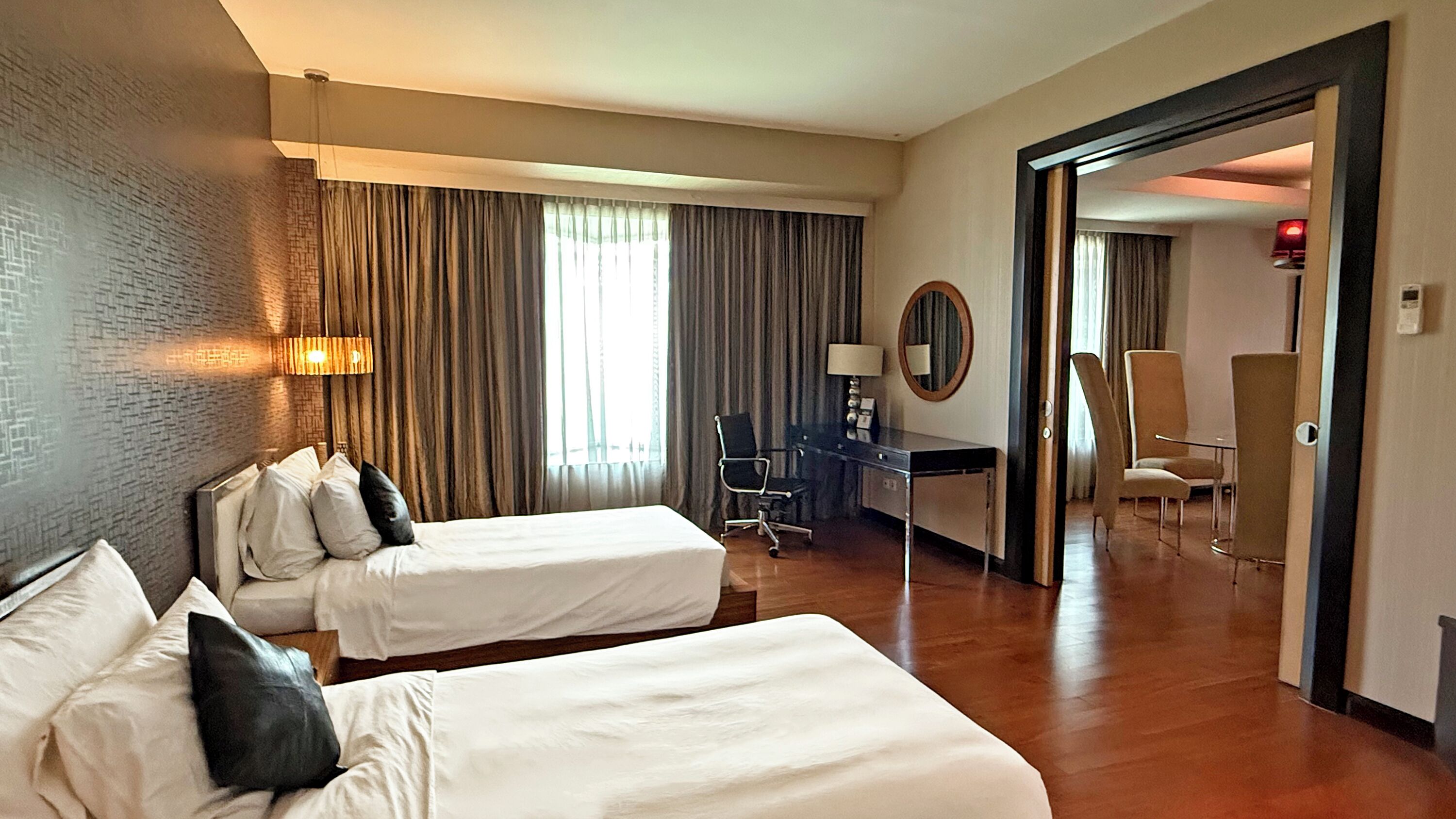 A hotel room with two beds, a desk, a chair, a mirror, and a door leading to another room.
