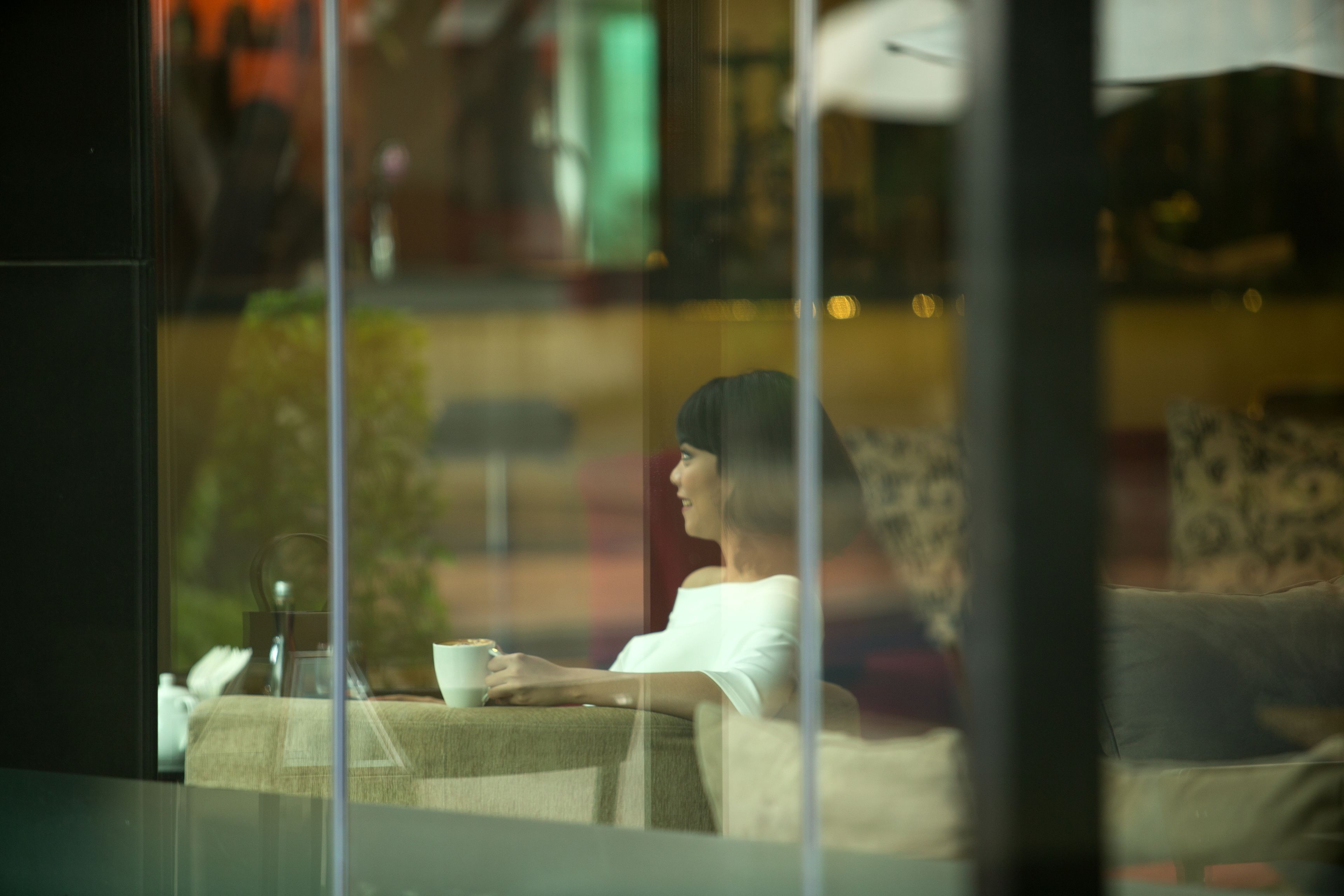 A person sitting by a window with a cup, a table with a glass, and a chair.