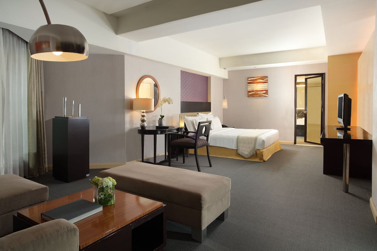 A hotel room with a bed, a desk, a chair, a sofa, a TV, and a lamp.