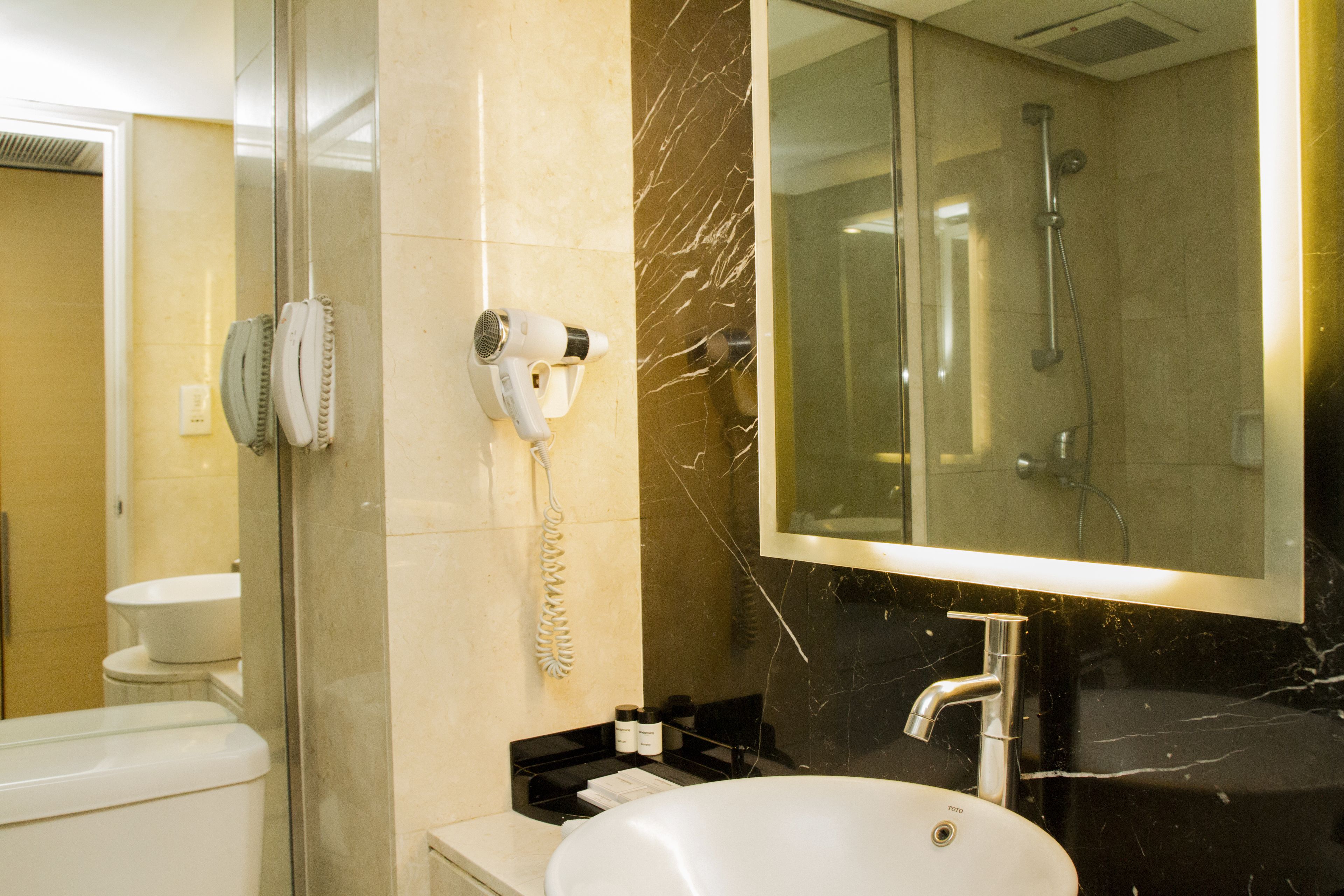 A modern bathroom with a glass-enclosed shower, a white sink, and a hairdryer mounted on the wall.