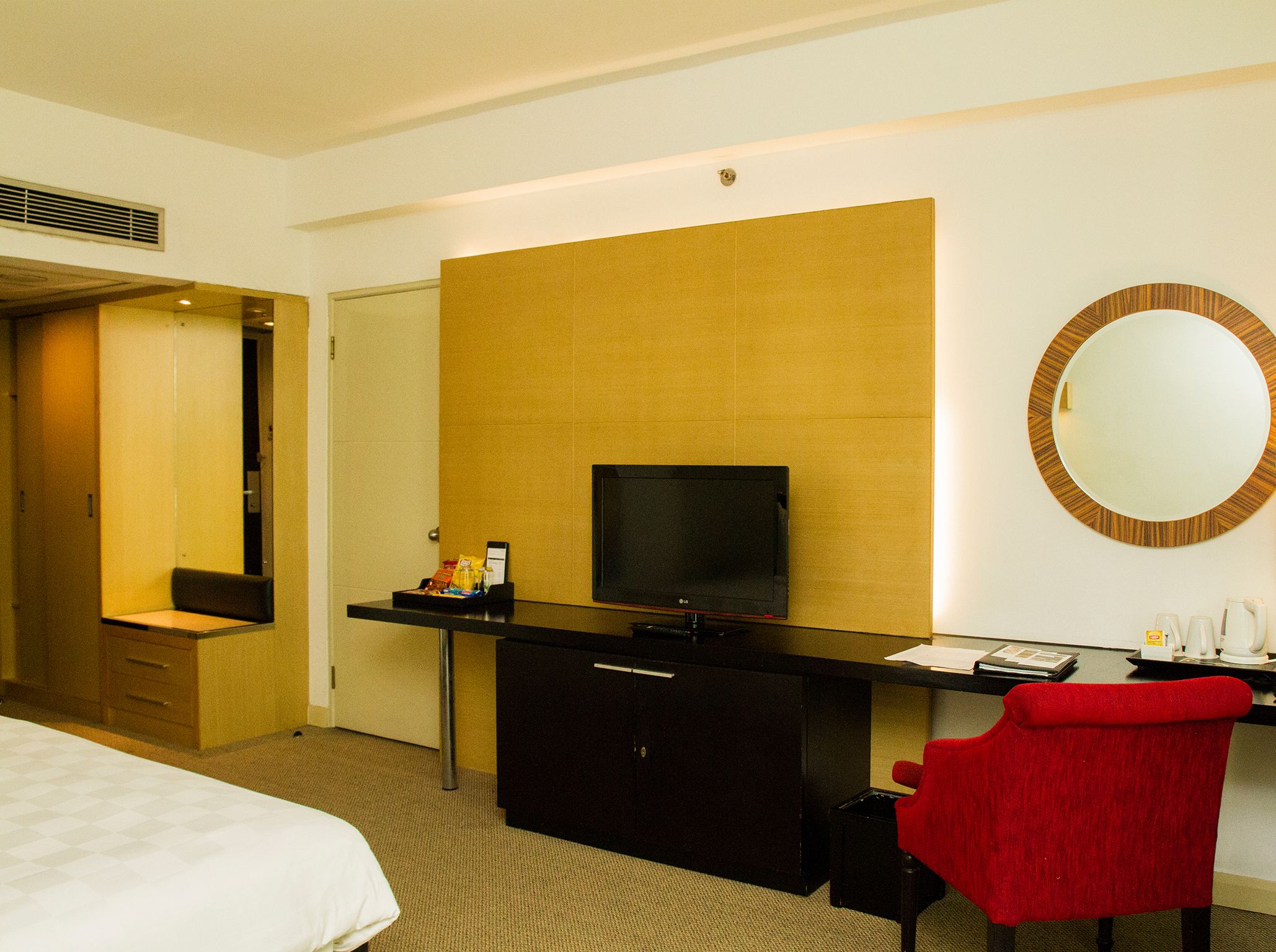Ein Hotelzimmer mit einem Bett, einem Schreibtisch mit Flachbildfernseher, einem roten Sessel, einem Spiegel und einer Minibar.