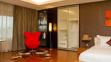 A modern hotel room with a large bed, a red chair, a wardrobe, and a glass door leading to a bathroom.