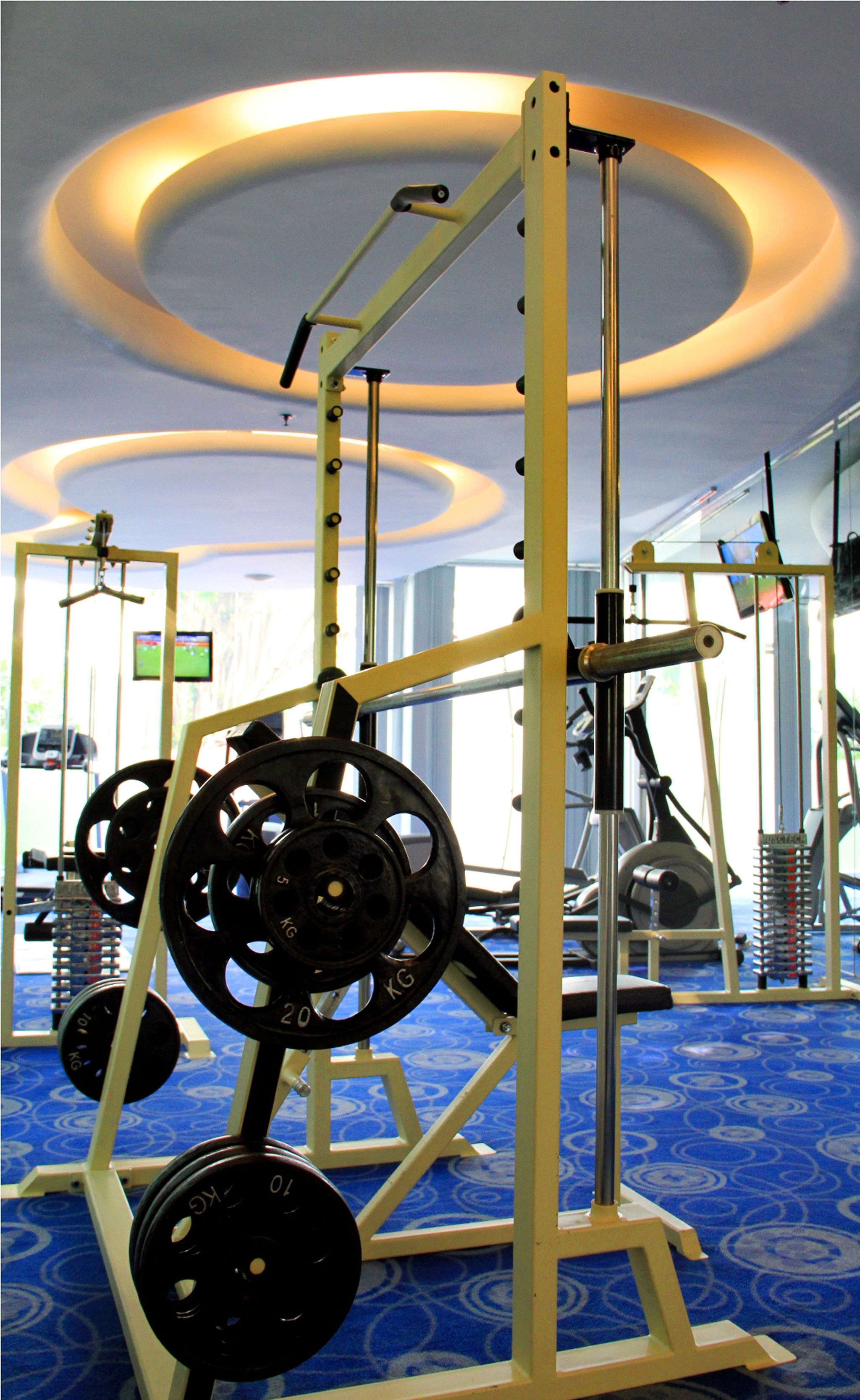 Ein Fitnessraum mit Krafttrainingsgeräten, einem blauen Teppich mit Muster und einer Decke mit runden Leuchten.