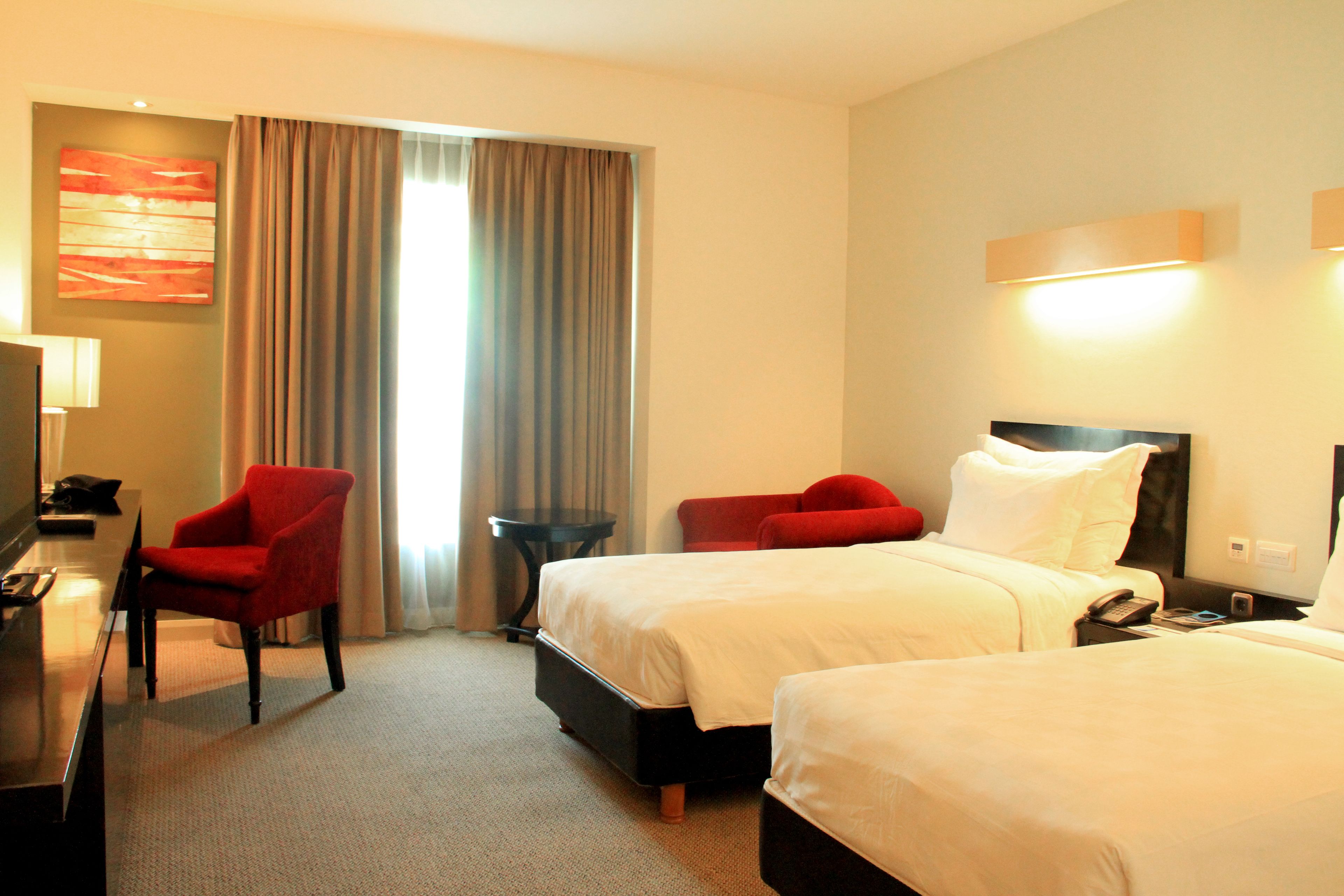 A hotel room with two beds, a desk with a chair, a TV, and a window with curtains.