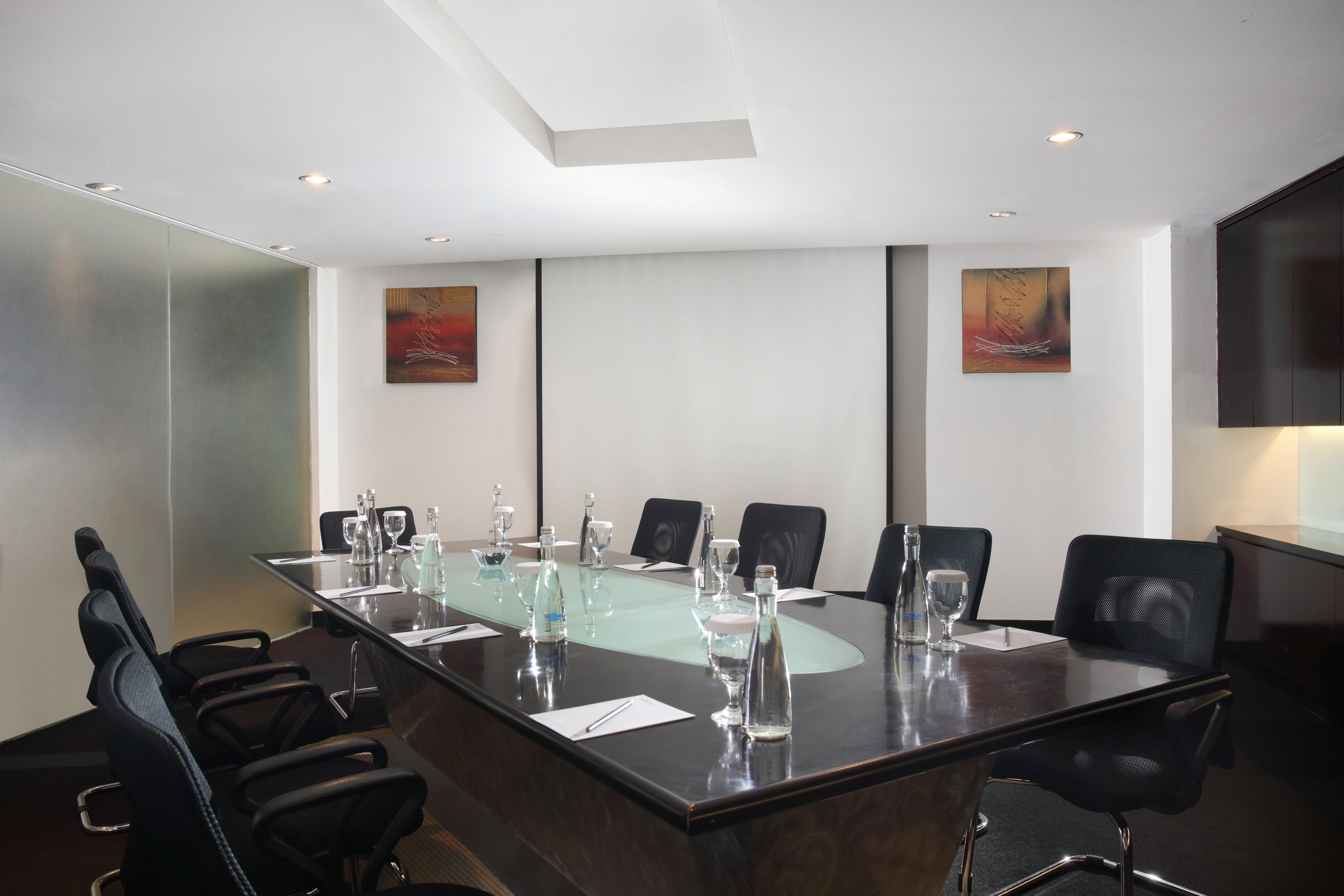 Une salle de conférence avec une table en verre, des chaises noires et deux tableaux accrochés aux murs.