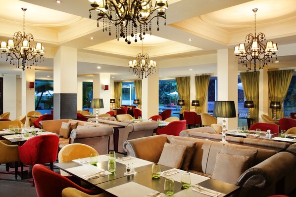 Un restaurante espacioso con varias zonas de comedor, candelabros y grandes ventanales.