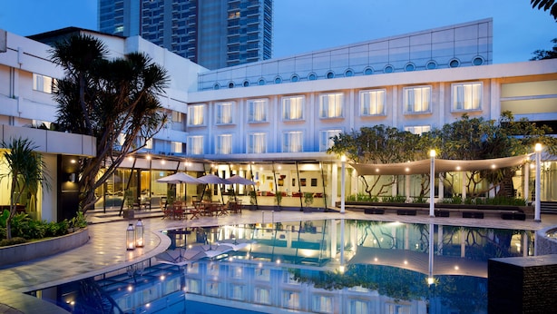 A modern hotel with a central pool, outdoor seating, and a well-lit terrace.