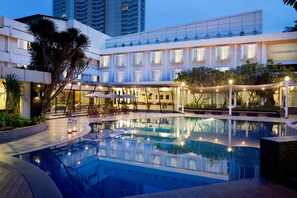 Un hotel moderno con piscina central, asientos al aire libre y una terraza bien iluminada.