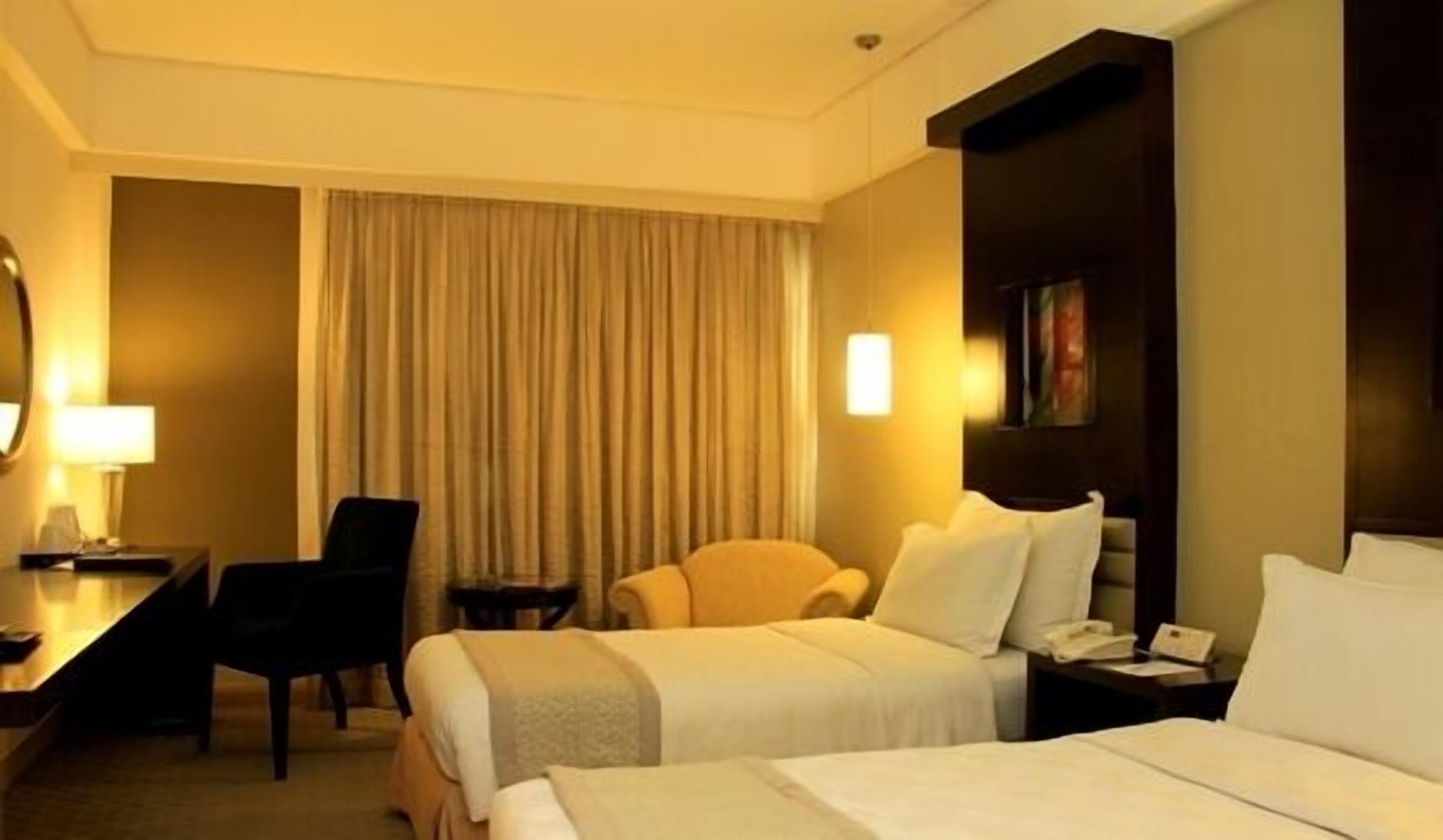 A hotel room with two beds, a desk, a chair, and a large window with curtains.